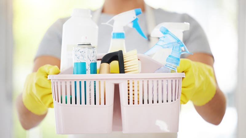 professional house cleaner holding cleaning supplies in a basket with gloves on